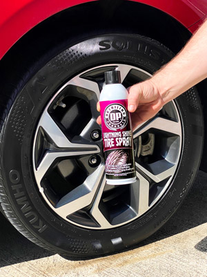 Image shows the tire with a high-gloss shine due to multiple layers of DP Lightning Shine Tire Spray being applied. The can of DP Lightning Shine Tire Spray is also being held by a hand in front of the wheel with the label showing. The holder of the can is off screen.